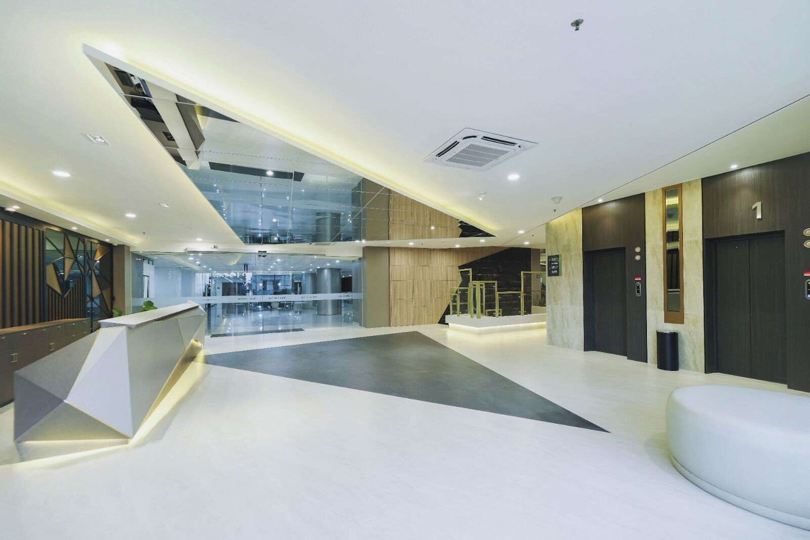A modern hotel lobby with a reception desk, a staircase, and a glass elevator.
