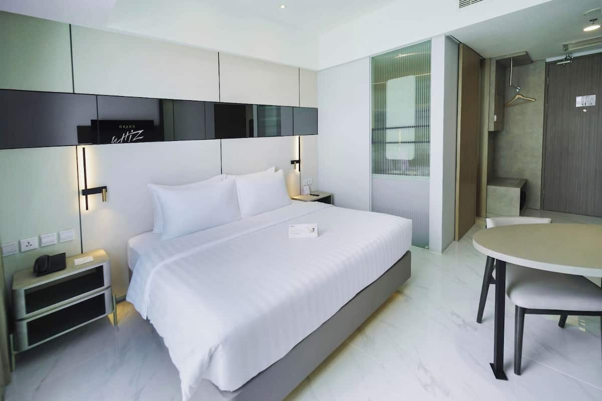 Una habitación de hotel moderna con una cama grande, mesitas de noche, un escritorio y un rincón de comedor.