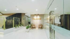 A modern lobby with a stone wall, a reception desk, and two wooden chairs. - Grand Whiz Hotel Praxis Surabaya (Surabaya)