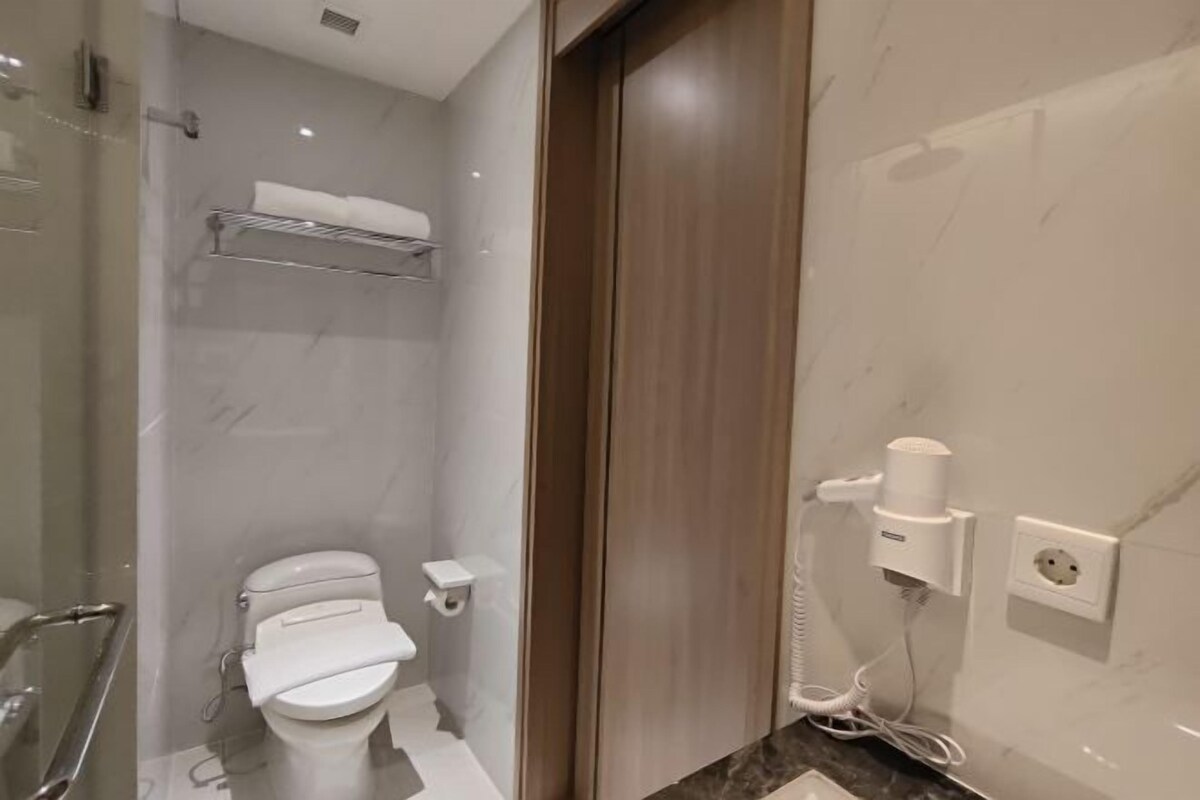 Un baño moderno con inodoro, ducha y secador de pelo montado en la pared.