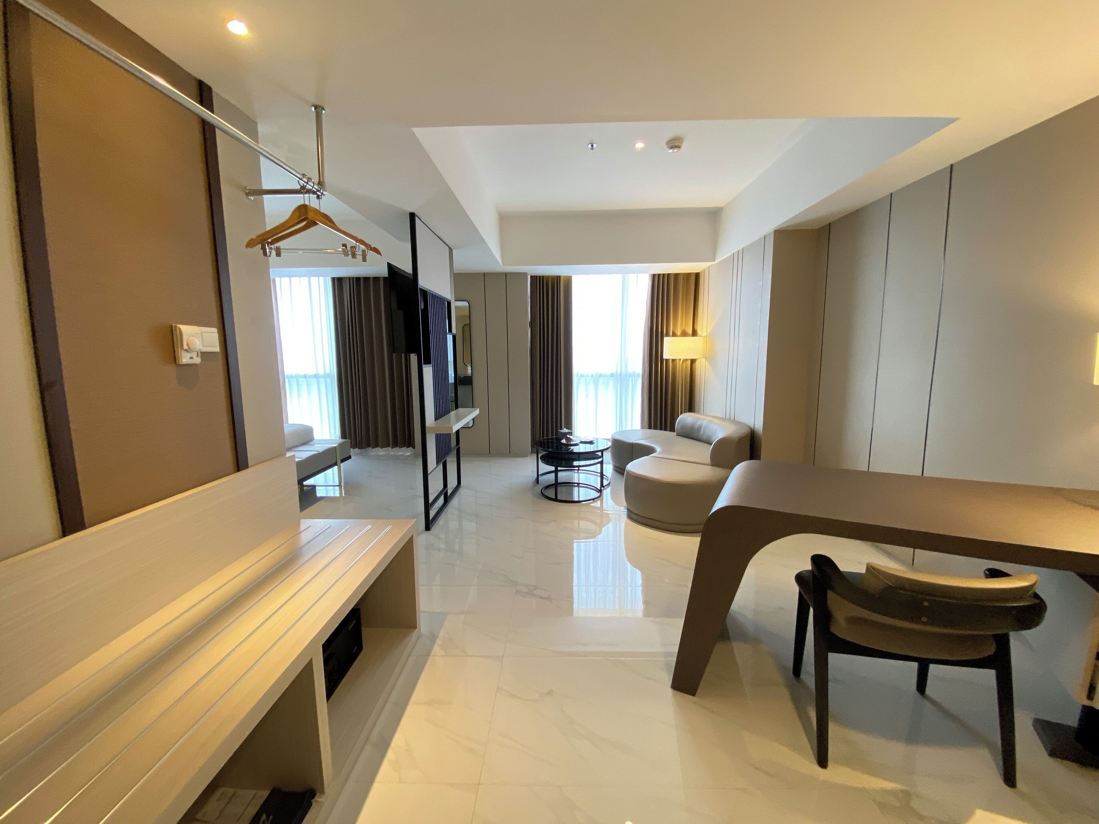A modern hotel room with a seating area, a TV mounted on the wall, and a dining table with chairs.