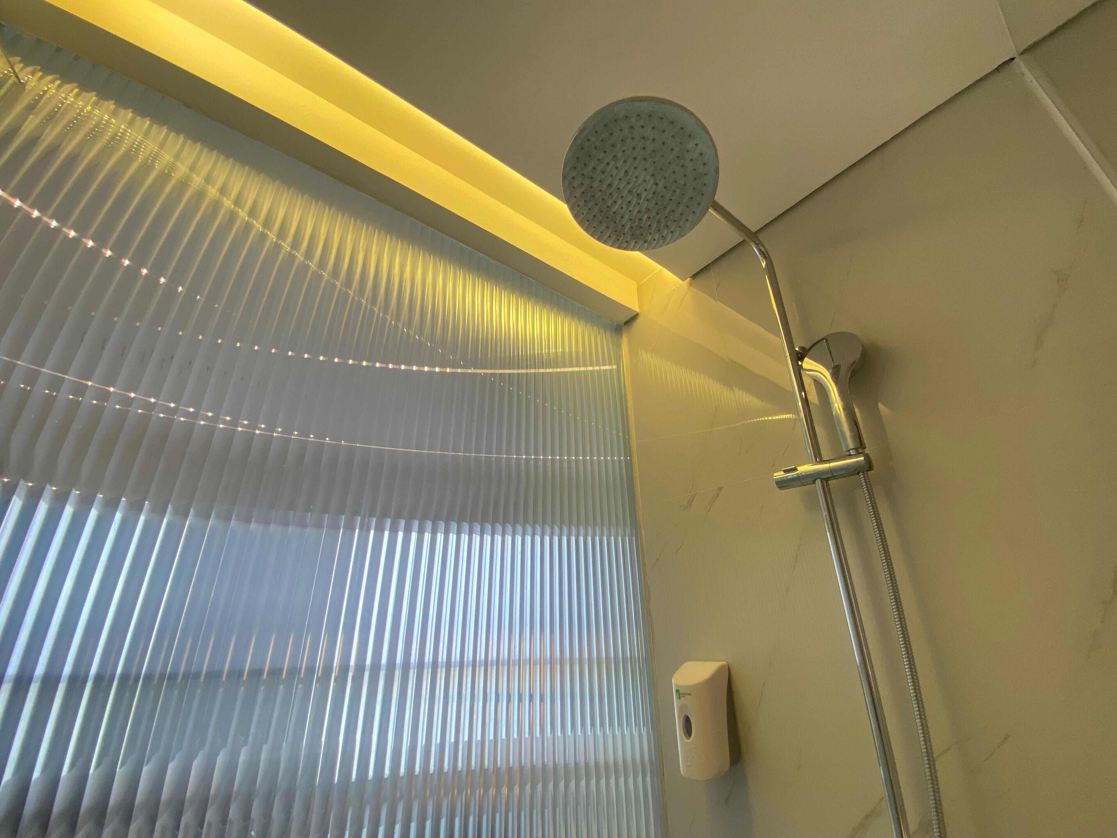 A shower with a handheld showerhead, a wall-mounted hand dryer, and a window with vertical blinds.