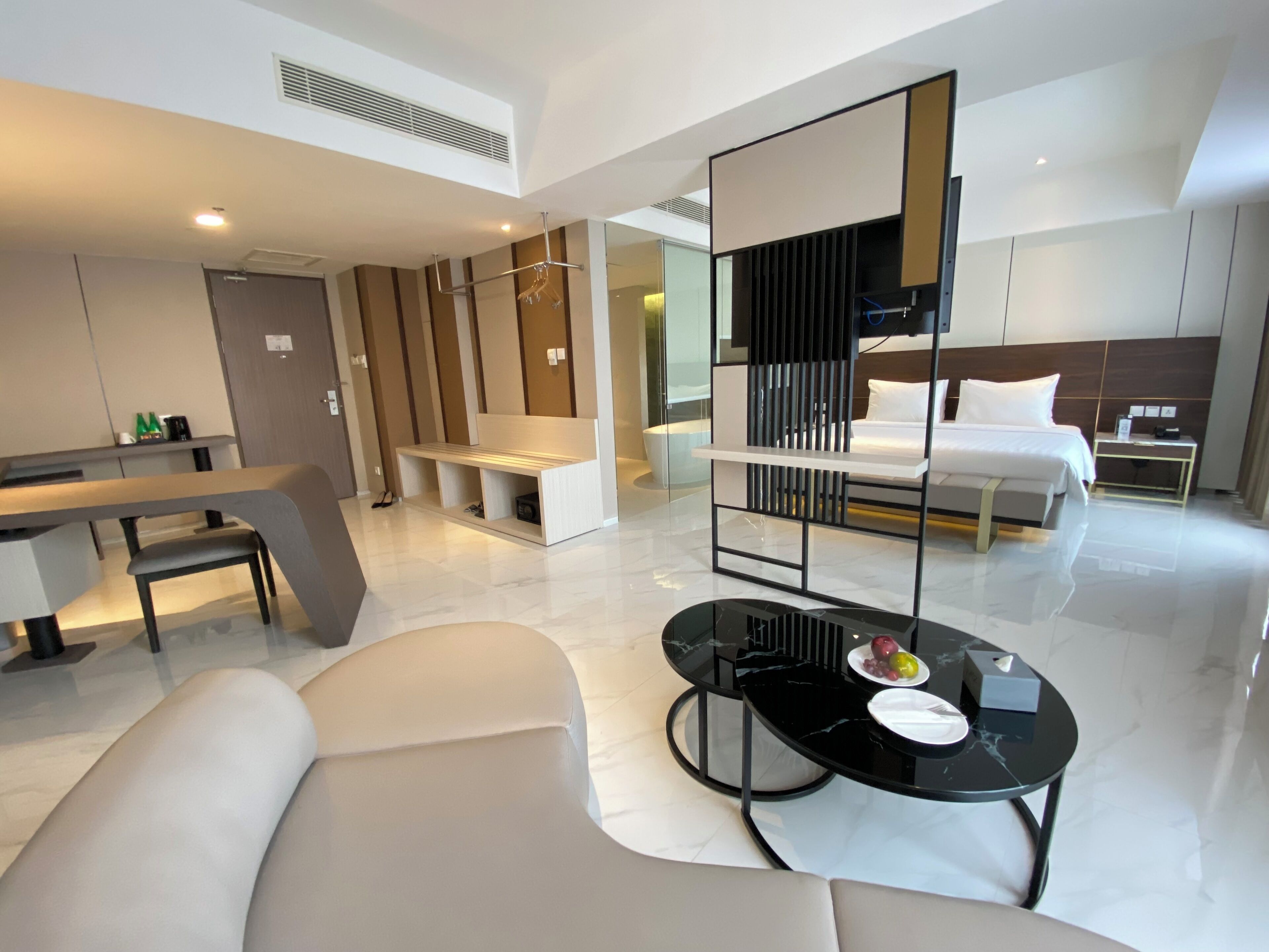 A modern hotel room with a dining area, a sofa, a bed, and a small table with a plate of fruit.