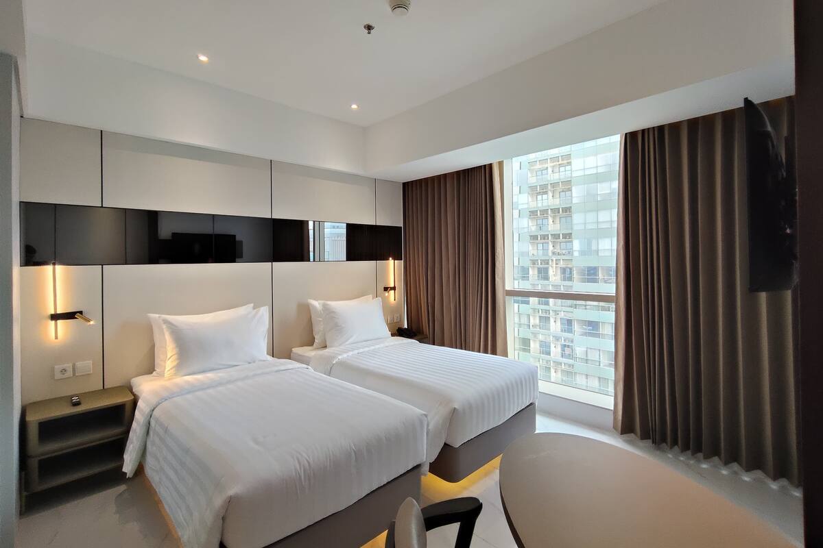 Una habitación de hotel moderna con dos camas, un ventanal con cortinas y vistas a la ciudad.