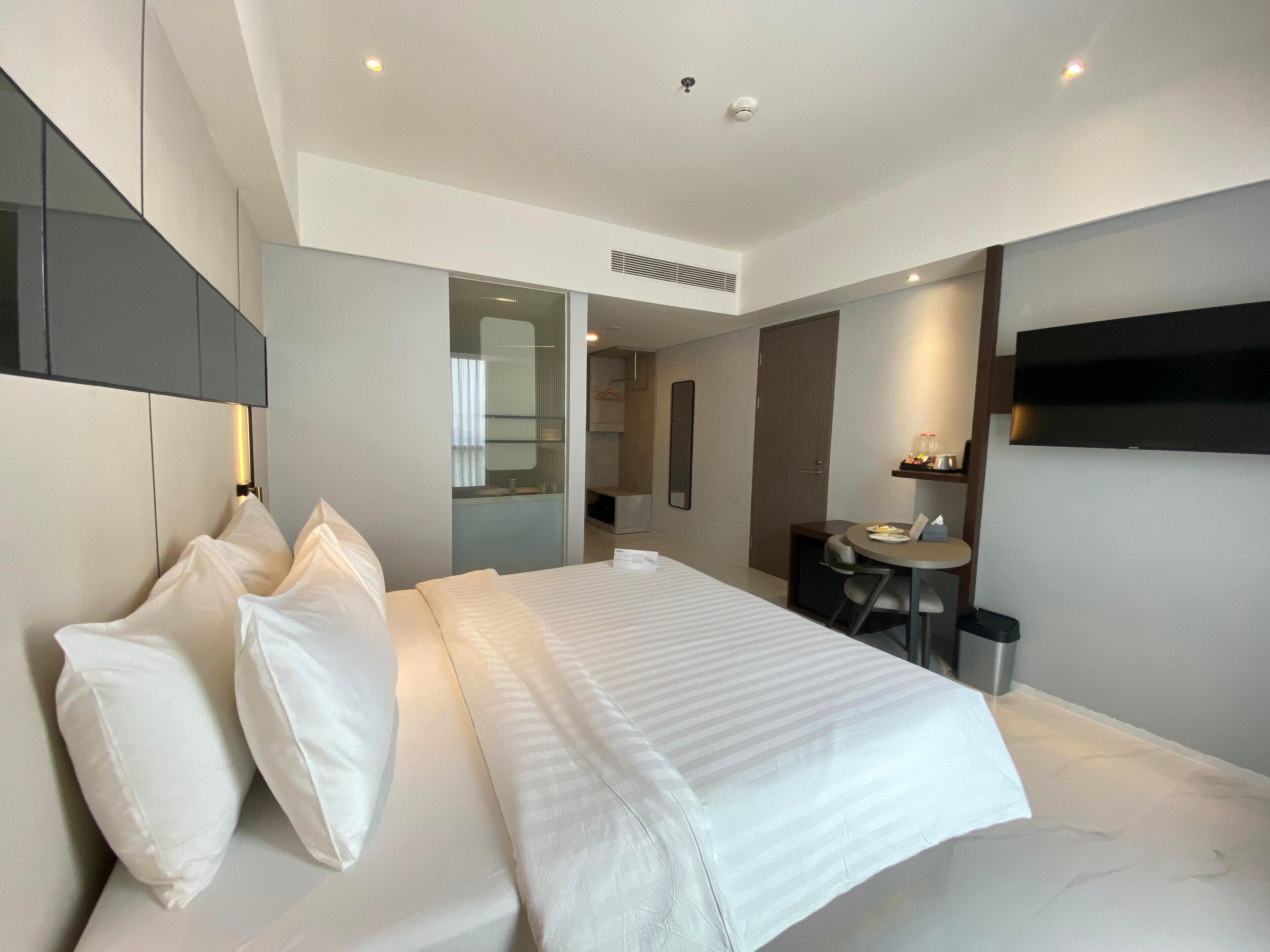 A modern hotel room with a large bed, a desk, and a TV.