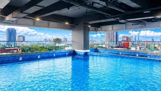 An indoor swimming pool with a cityscape view, supported by metal beams and pillars. - Grand Whiz Hotel Praxis Surabaya (Surabaya)