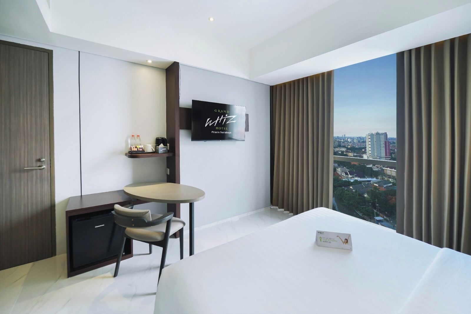 Ein modernes Hotelzimmer mit einem großen Bett, einem kleinen Schreibtisch mit Stuhl, einem Fernseher und Blick auf die Stadt.