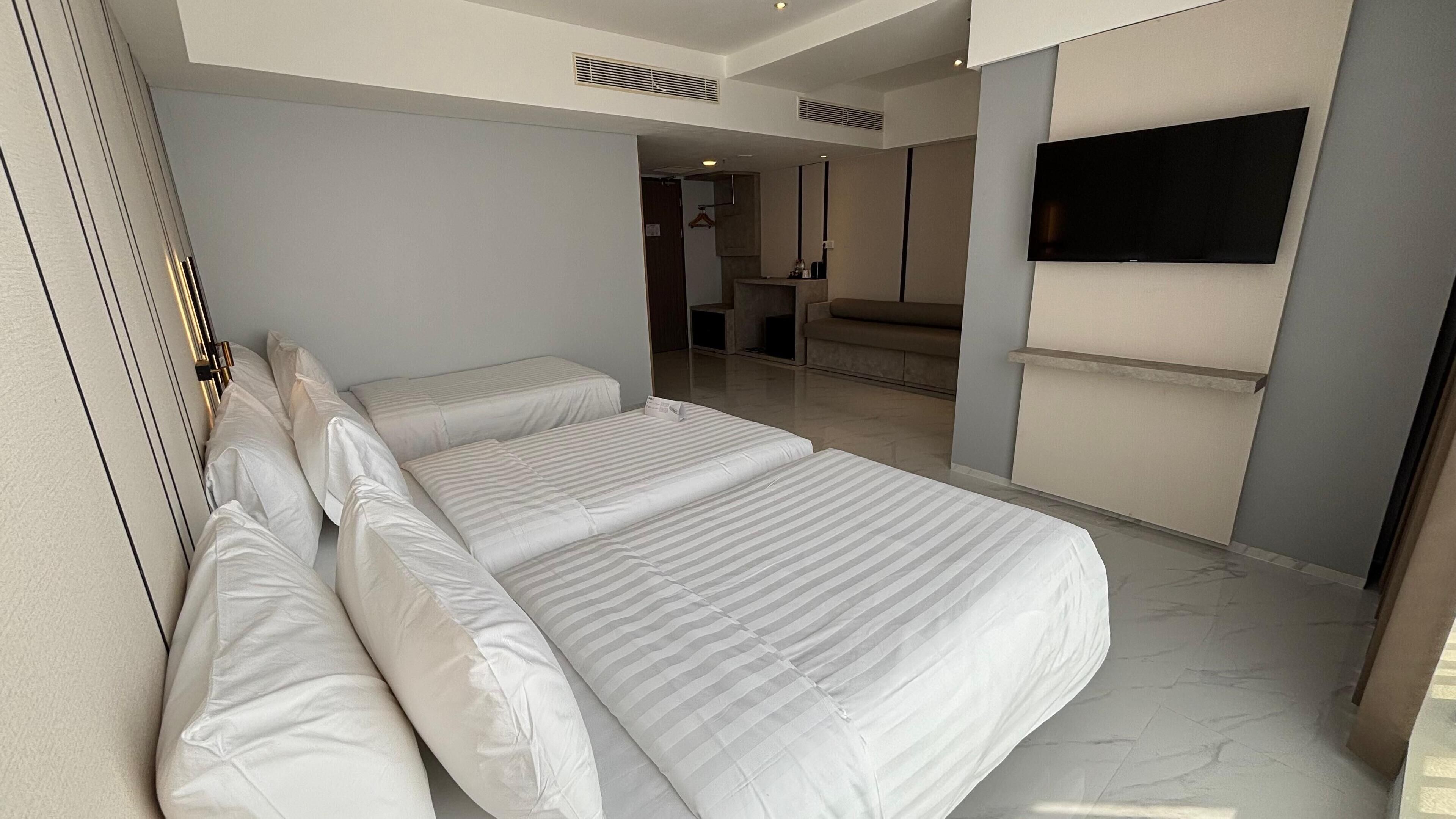 Una habitación de hotel moderna con una cama grande, un televisor montado en la pared y un baño visible a través de una puerta abierta.