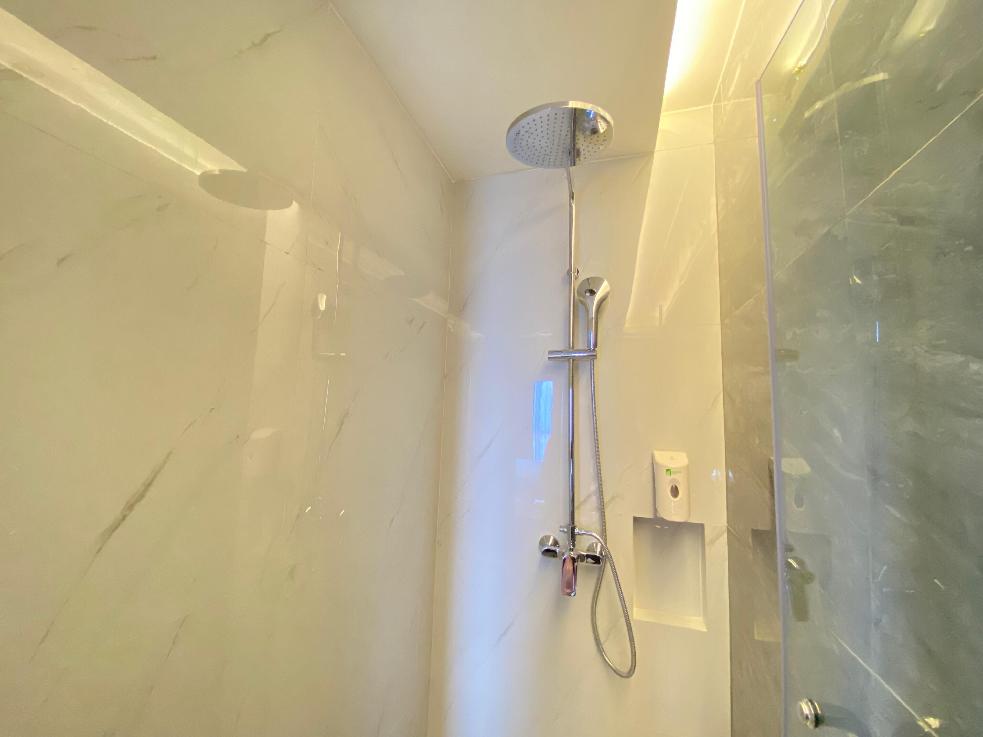 A modern bathroom with a glass shower enclosure, a handheld showerhead, and a wall-mounted control panel.