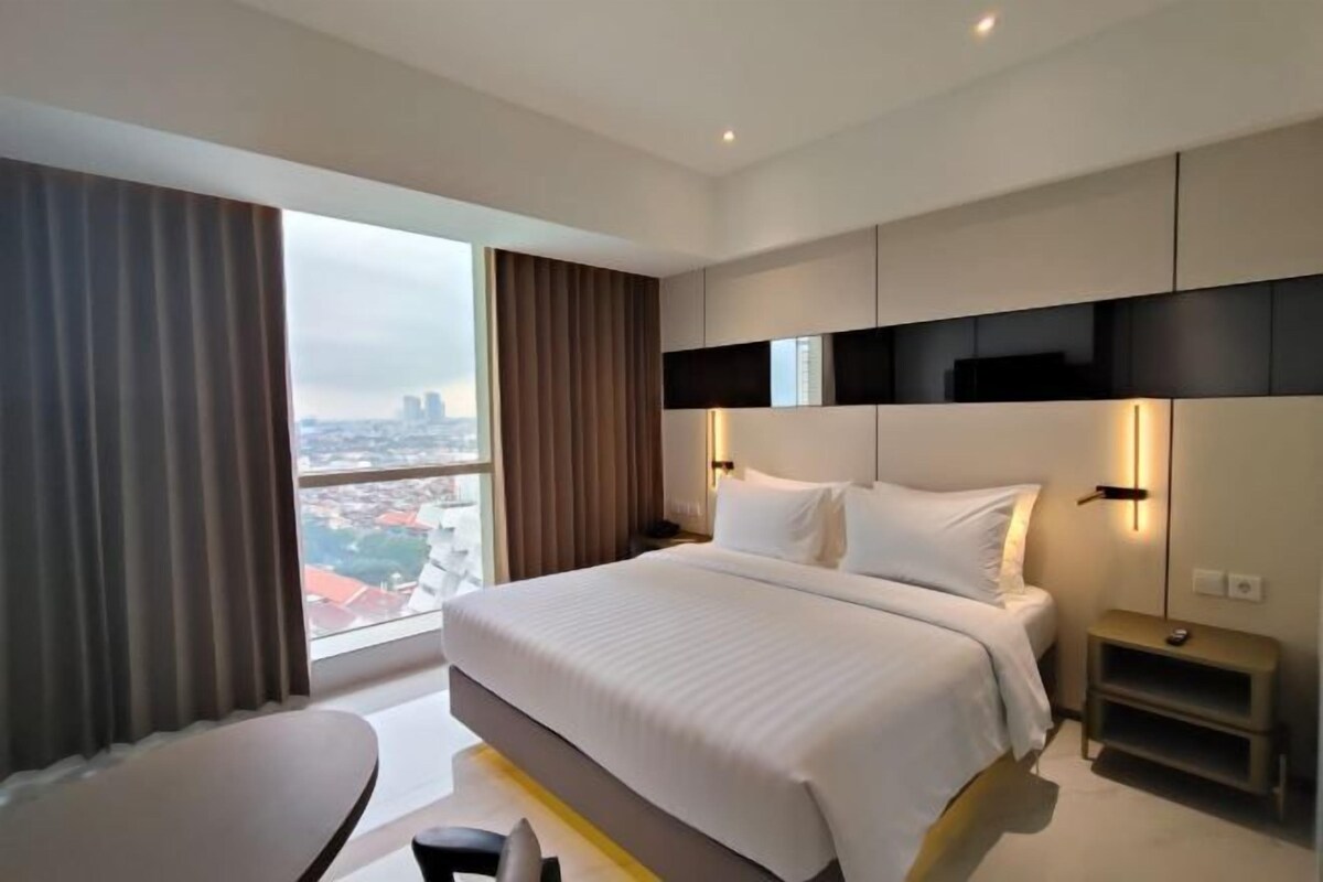 Una habitació d'hotel moderna amb un llit gran, un escriptori i vista a la ciutat.