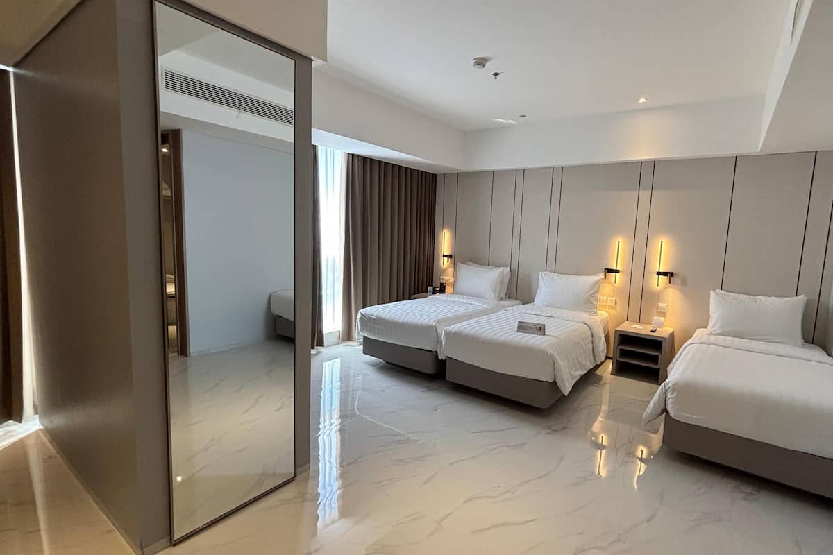 Habitación de hotel moderna con dos camas, un espejo grande y una puerta corredera que da a otra habitación.