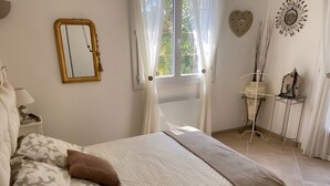 A bedroom with a bed, a nightstand, a mirror, a window with curtains, and a small table with decorative items. - NEW! VILLA LORANA Between sea and vineyards (SAINT CYR)