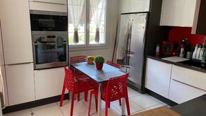 A compact kitchen with white cabinets, a built-in oven, a refrigerator, and a dining table with red chairs. - NEW! VILLA LORANA Between sea and vineyards (SAINT CYR)