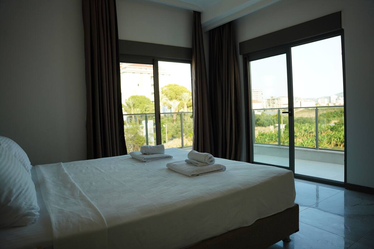 A hotel room with a large bed, two towels, and a balcony with a city view.
