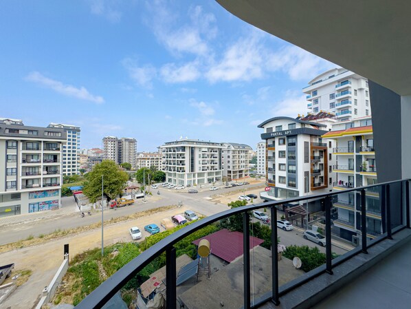 A view from a balcony overlooking a cityscape with modern apartment buildings, a parking area, and a clear sky.