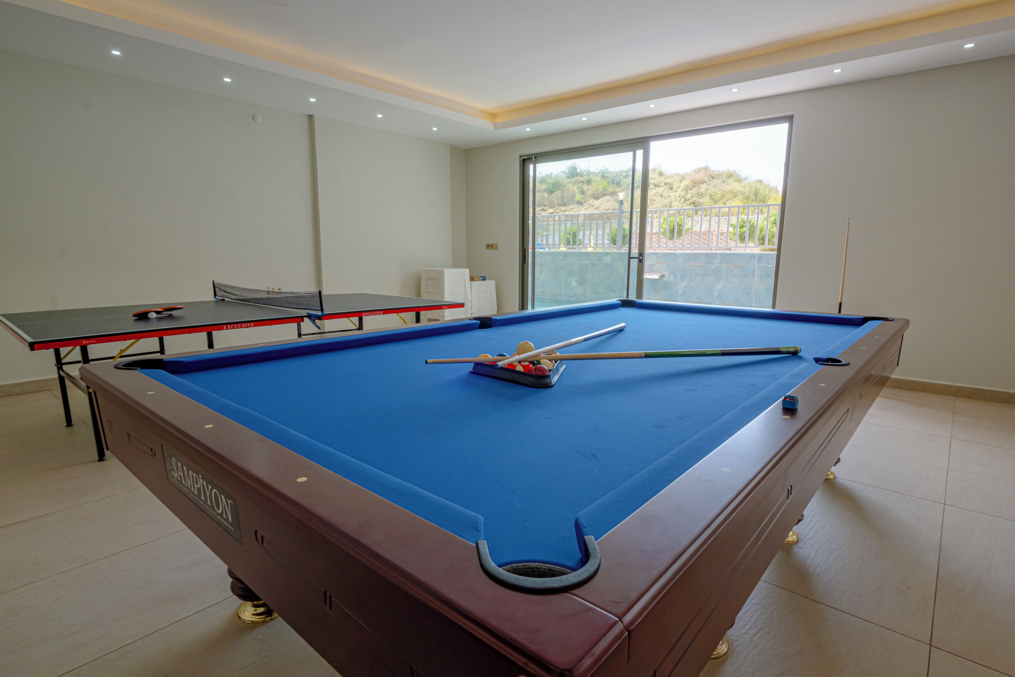 A pool table with a blue felt surface, a red table tennis table, and a billiard cue.