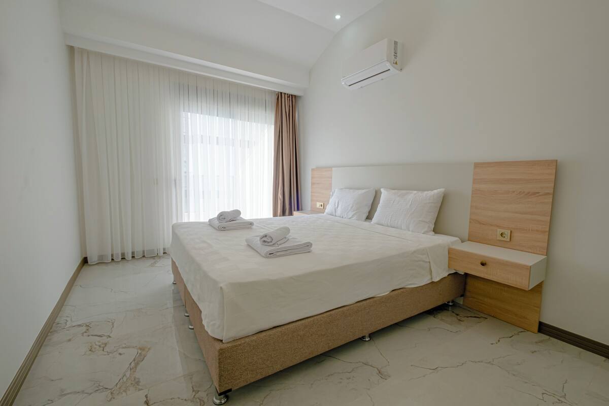 A modern hotel room with a large bed, a wooden nightstand, and a built-in headboard.