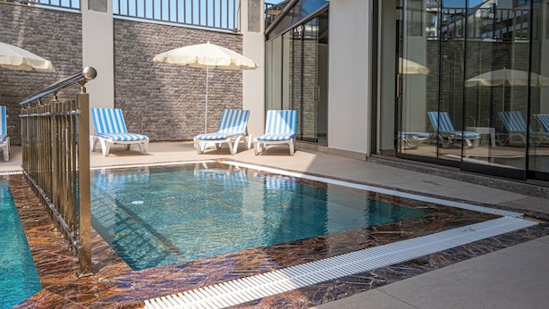 A swimming pool with blue and white striped lounge chairs and umbrellas, surrounded by stone walls and glass doors.