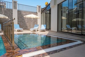 A swimming pool with blue and white striped lounge chairs and umbrellas, surrounded by stone walls and glass doors.
