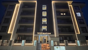 A modern hotel building with illuminated signage reading "INCIsuites" and a sign for "INCIsuites & Tatil Evleri".