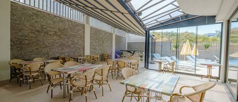 A spacious indoor area with tables and chairs, large windows, and a view of outdoor seating.