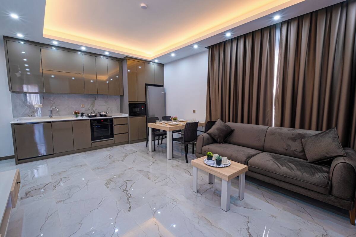 A modern kitchen with built-in appliances, a dining area with a table and chairs, and a living area with a sofa and a coffee table.