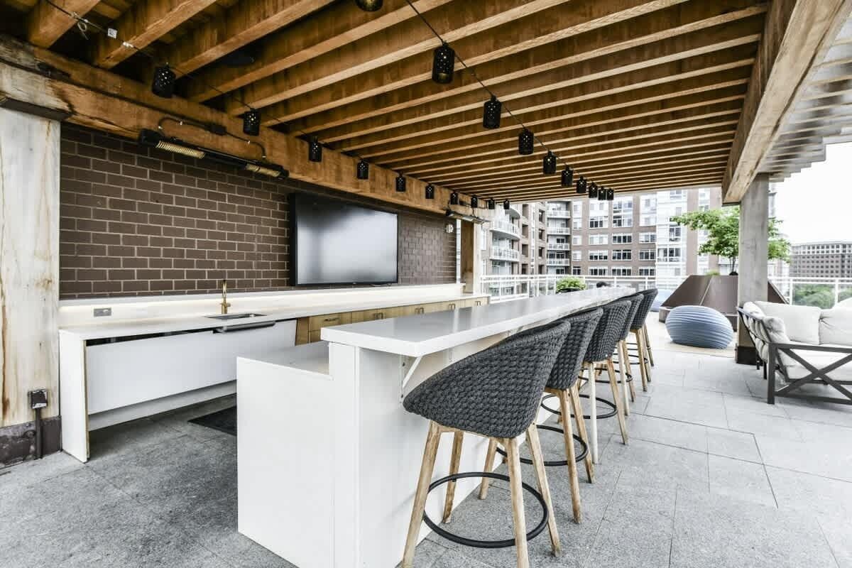 A modern outdoor kitchen area with a brick backsplash, white countertops, and bar stools.
