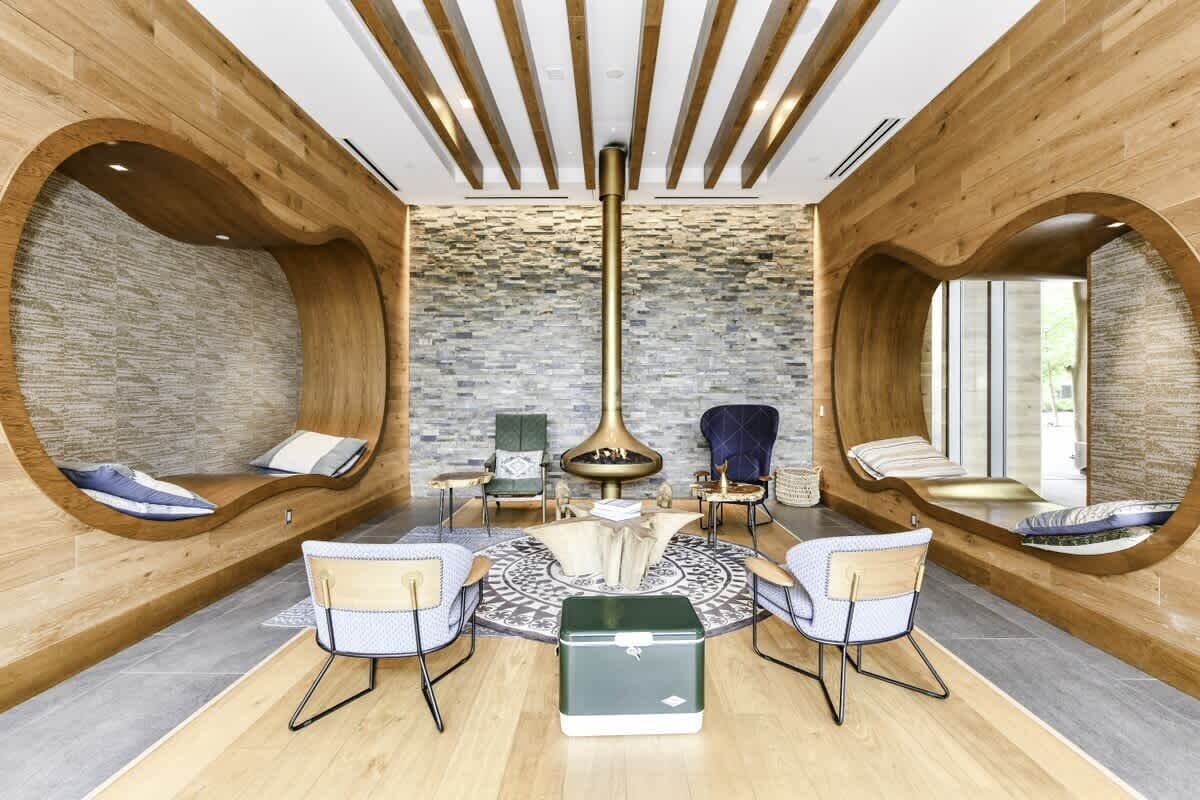 A modern lounge with wooden walls, a central fire feature, and seating areas.