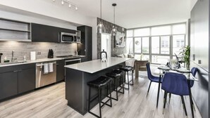 A modern kitchen with a central island, bar stools, and a dining area with blue chairs. - Modern 2BR Escape with Gym, Parking & Airport Views (Arlington)