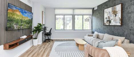 Una sala de estar moderna con un televisor grande, un sofá, una mesa de centro y un ventanal amplio.