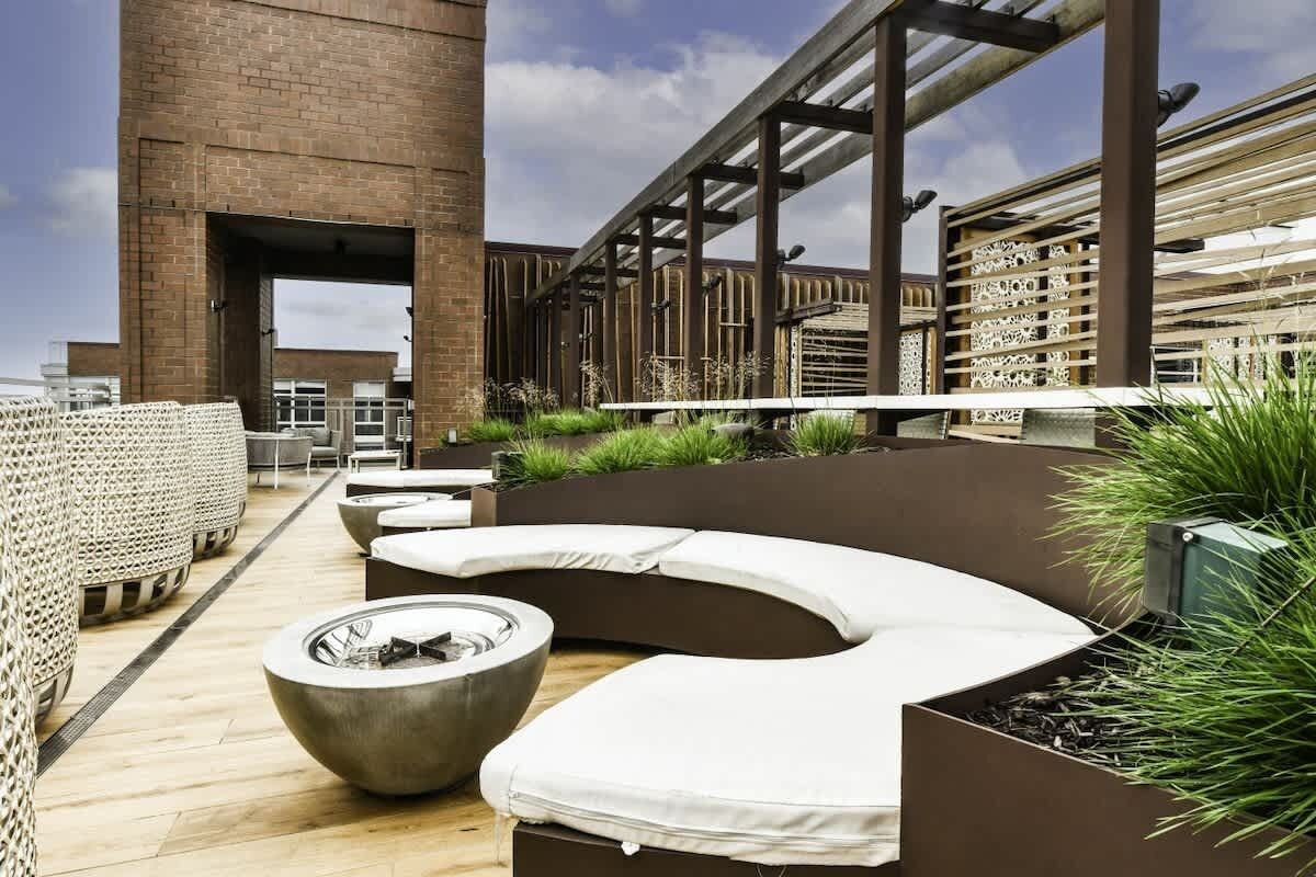 A rooftop terrace with a curved seating area, a fire pit, and a view of the cityscape.
