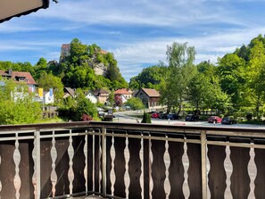 A balcony with a view of a town, including houses and a castle on a hill. - Forellenhof (Pottenstein)
