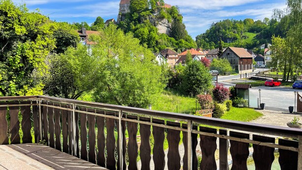 A balcony with a view of a residential area, including houses and a hill with a building on top. - Forellenhof (Pottenstein)