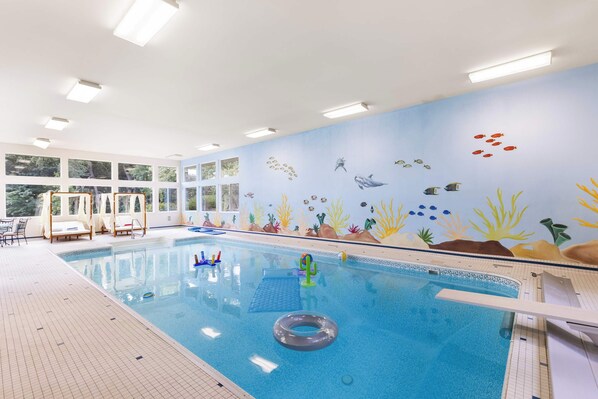 Une piscine intérieure ornée d’une fresque représentant un paysage sous-marin, avec une eau cristalline et un sol carrelé.