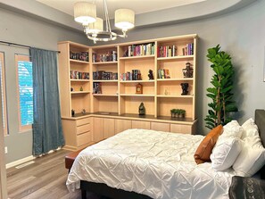 Une chambre avec un grand lit, une bibliothèque intégrée, un bureau et une plante en pot.