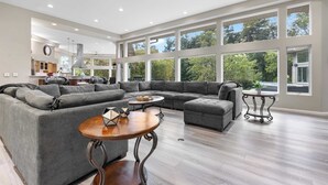 A spacious living room with a sectional sofa, a round wooden coffee table, and a large window offering a view of the outdoors. - Wembley Place Estate/Indoor Pool/Hot Tub/Game Room (Rockford)