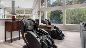 A spacious room with a massage chair, a small table with decorative items, and large windows offering a view of trees. - Wembley Place Estate/Indoor Pool/Hot Tub/Game Room (Rockford)