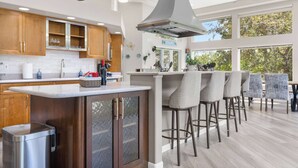 A modern kitchen with wooden cabinets, a stainless steel trash can, and a bar area with stools. - Wembley Place Estate/Indoor Pool/Hot Tub/Game Room (Rockford)