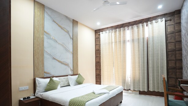 A modern bedroom with a large bed, a nightstand, a chair, and a ceiling fan. - Hotel Saina Stay Inn (Gurugram)