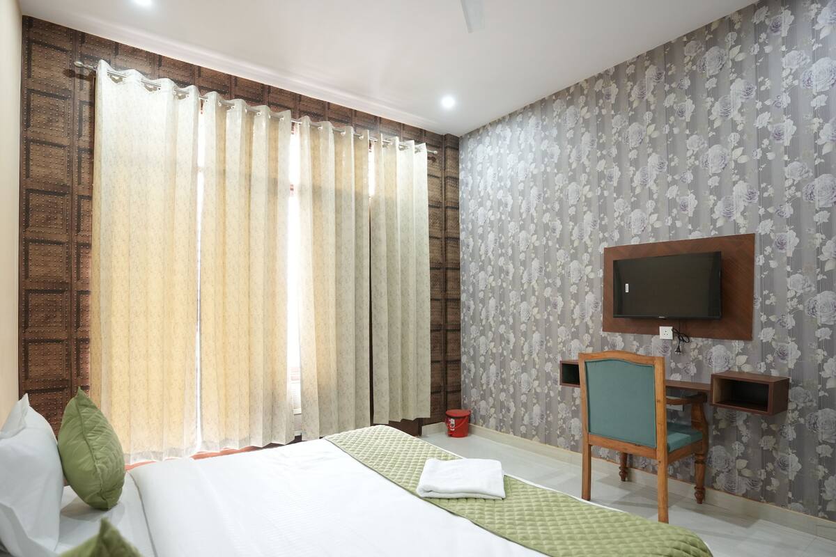 A hotel room with a bed, curtains, a TV, a desk, and a chair.