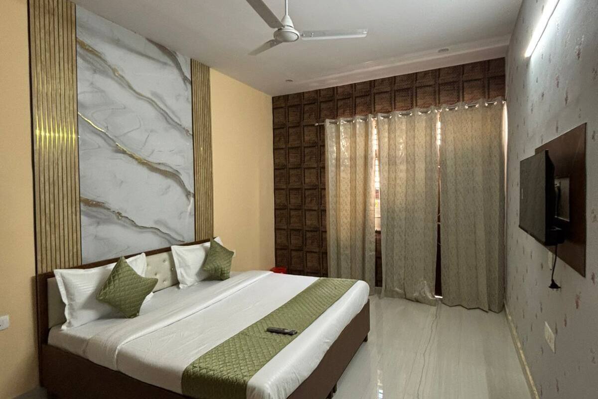 A bedroom with a bed, a ceiling fan, a TV mounted on the wall, and a window with curtains.