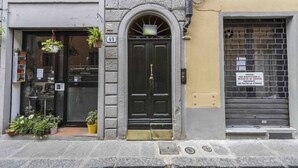 Un edifici amb una porta negra, una finestra amb un rètol i un persianer tancat a la dreta.