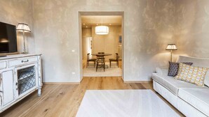 Un saló amb un sofà blanc, un televisor sobre un moble blanc, una zona de menjador amb taula i cadires, i un passadís que condueix a una altra habitació.
