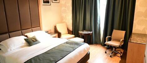 A hotel room with a large bed, a desk, a chair, and a small table.