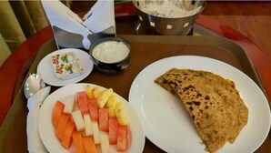 Un plateau avec une assiette de salade de fruits, un bol de yaourt et une galette pliée.
