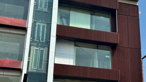 Un immeuble à plusieurs étages doté d’une façade moderne, comprenant une agence bancaire bien visible, un hôtel et une voiture garée devant.