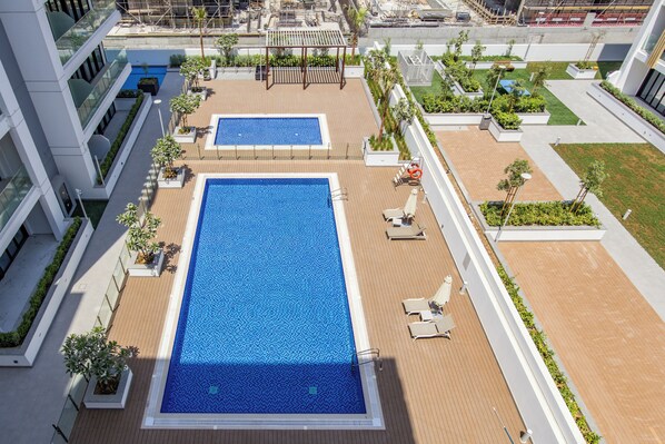 A rooftop pool area with two pools, lounge chairs, and a pergola.