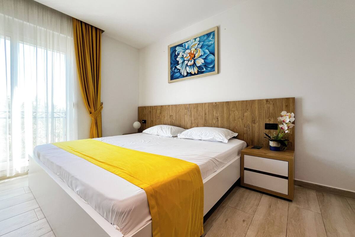 Een hotelkamer met een bed, een nachtkastje, een schilderij en een raam met gordijnen.