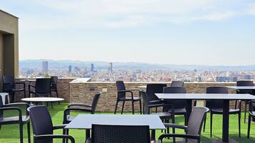 An outdoor seating area with tables and chairs, a view of a cityscape, and a stone wall.