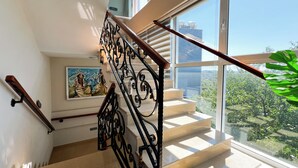 A staircase with ornate black railings, a painting on the wall, and a view of greenery outside. - Jata Hotel (Tirana)